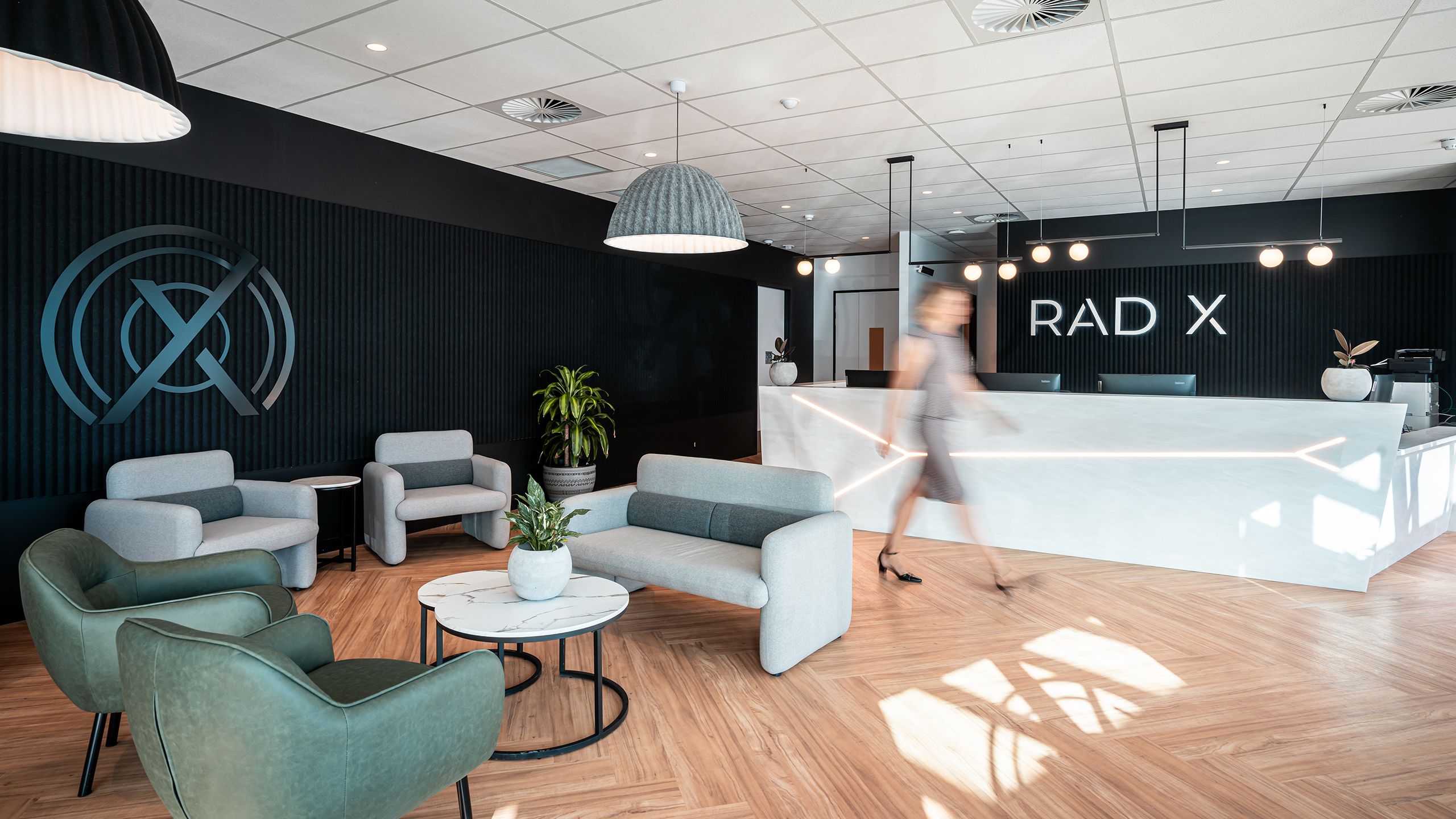 Inside the reception of the Rad X clinic in Hobart, a staff member walks through the room, there are plush couches and soft lighting.