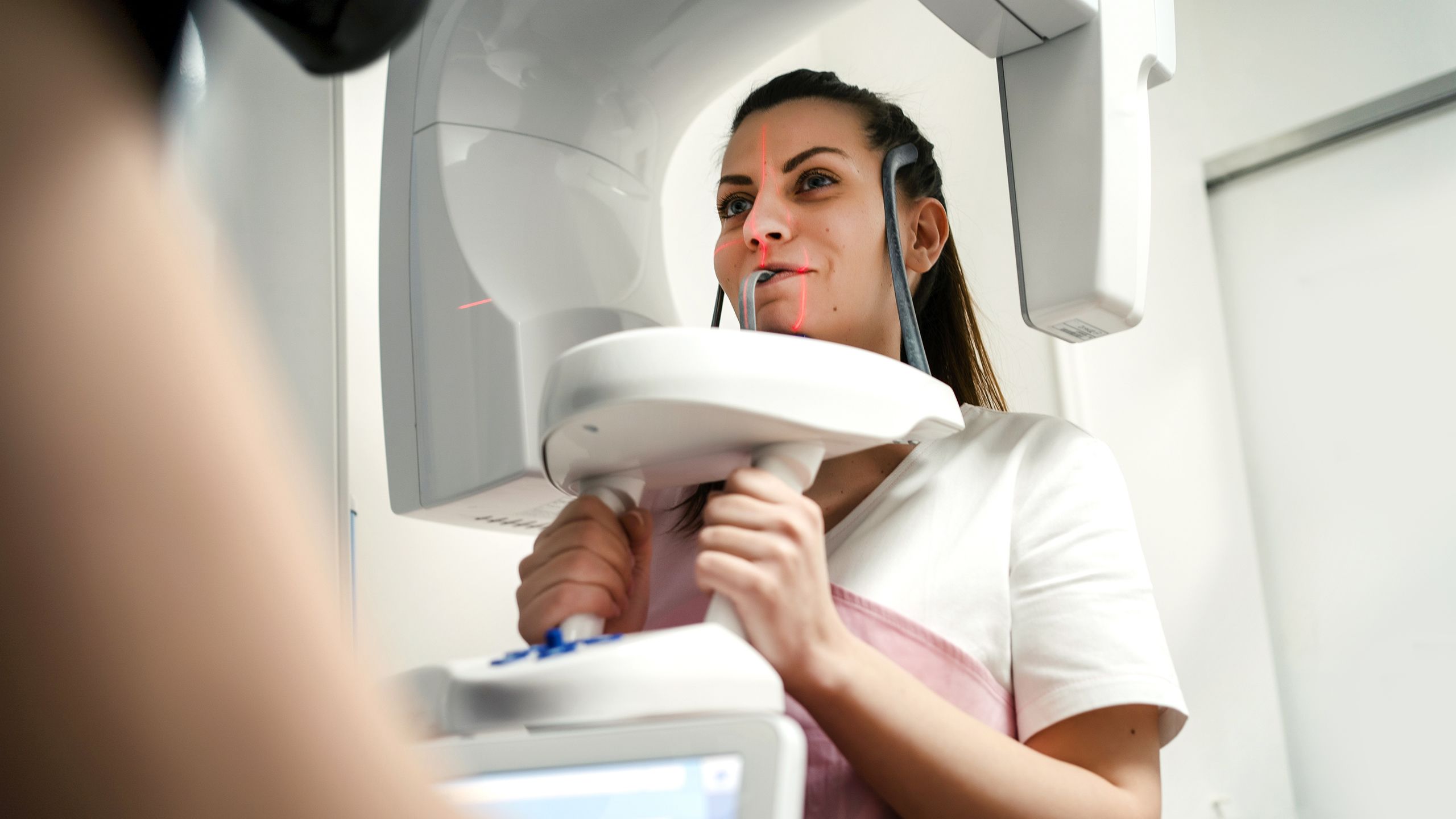 a woman has her head in a 360 dental x-ray machine. She has her mouth on a rod that comes out of the machine. 