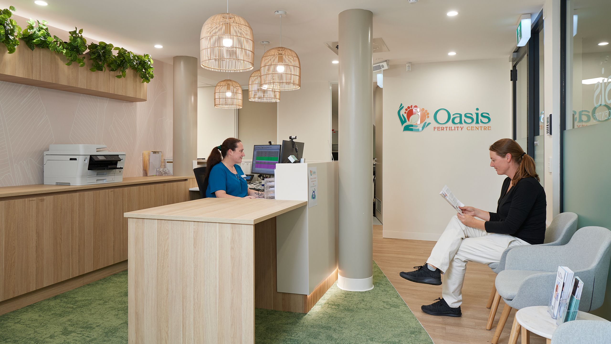 The Oasis Fertility Centre reception including a female receptionist sitting at a desk and a female patient waiting on a chair in the waiting room. 
